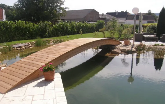 Geschwungene Holzbrücke über einen Schwimmteich